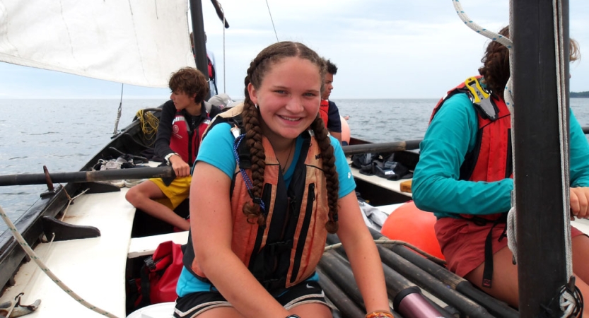 a person wearing a life jacket smiles at the camera while sitting on a sailboat